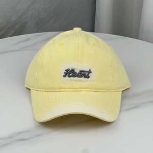 Close-up of yellow cotton baseball cap with gray Heart embroidery on marble background