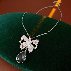 Detail of silver bow necklace with pink rhinestones and dark teardrop gemstone on green velvet