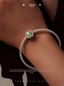 Close-up of a silver mesh bracelet with a green clover pendant worn on the wrist