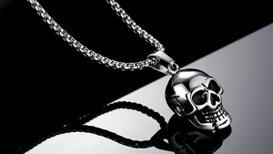 Macro shot of silver metal skull pendant with round box chain on reflective surface