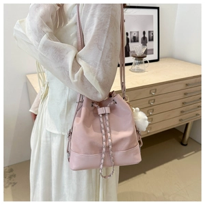 Pink drawstring bucket bag with chain strap and soft pompom charm detail on model