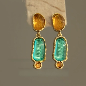 Detailed shot of resin drop earrings with irregular amber and green stones in gold setting