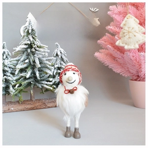Plush Christmas gnome with knitted hat and bell standing by a festive snowy pine tree