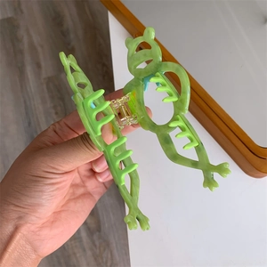Makroaufnahme der grünen Frosch-Haarklammer mit Textur und goldener Metallfeder