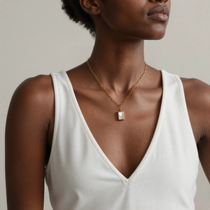 Détail d'un collier doré avec pendentif rectangulaire en nacre porté sur la clavicule fine