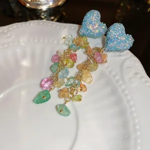 Macro detail of long tassel earrings with colorful resin stones and glitter heart studs