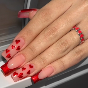 Long coffin fake nails with red glitter french tips and heart patterns on nude base