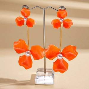 Detailed close-up of orange floral drop earrings with pearls on a professional display stand