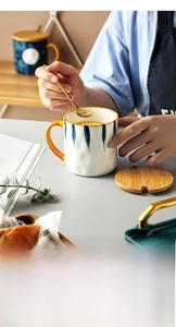 Detail of hand stirring coffee in a blue striped ceramic mug with wooden lid and golden spoon