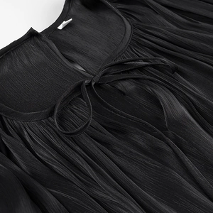 Macro shot of the black pleated neckline featuring a delicate bow tie and ruffle detail