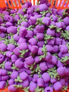 Detailed pile of rose-shaped silicone beads with purple petals and green base in a container