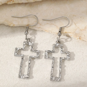 Macro shot of silver hollow cross earrings with hammered texture on stone background