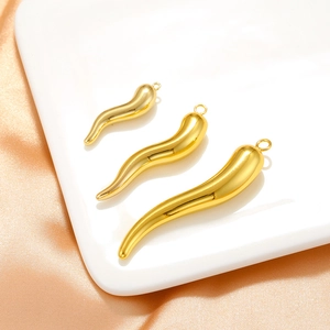 Detailed view of three polished gold chili pendants in various sizes on silk background