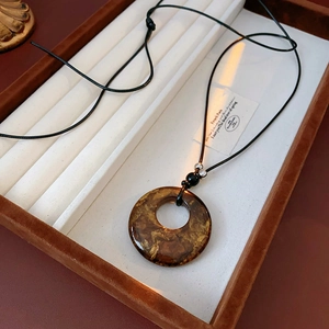 Macro shot of amber resin circular hollow pendant with golden texture and black cord