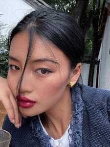 Close-up of elegant gold heart-shaped earrings worn by a model in a navy tweed jacket