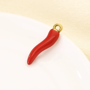 Macro shot of a glossy red chili pepper pendant with a gold ring on a white plate