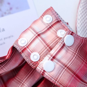 Detailed close-up of red plaid fabric texture and white plastic snap button on pet vest