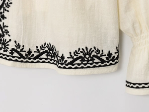 Gros plan de broderies florales noires sur tissu lin crème avec bords ondulés