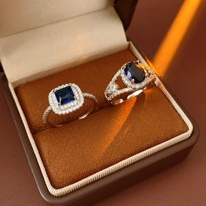 Detailed view of silver zircon rings with blue square and oval gemstones in a box