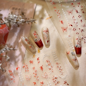 Detail of champagne gold nails with red butterflies and white bamboo leaf nail stickers
