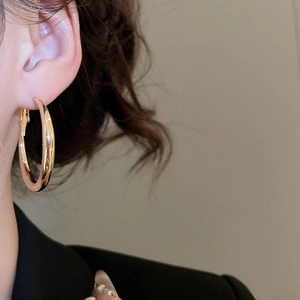Close-up of a model wearing minimalist gold C-shaped geometric hoop earrings