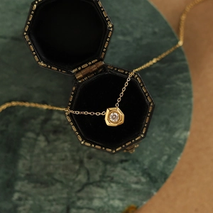 Detailed close-up of a hexagonal gold pendant with a sparkling white diamond on a gift box