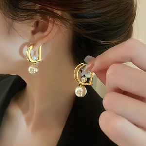 Macro view of gold D-shape pearl earrings on model highlighting the elegant metal luster
