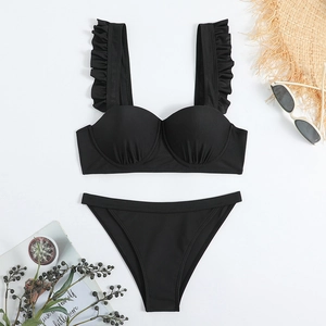Flat lay of black bikini with ruffle straps and underwire cups on summer vacation props