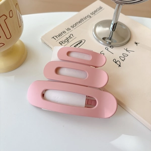 Detailed view of three matte pink oval hair clips on a white card display