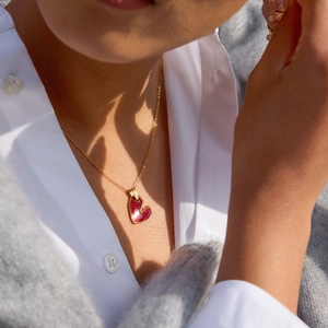 Dettaglio di una collana con pendente a cuore rosso e catena dorata su modella