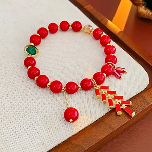 Détail du bracelet à perles rouges avec breloque pétard doré et anneau de jade