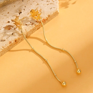 Detail of gold sunburst drop earrings with snake chains on a textured stone base