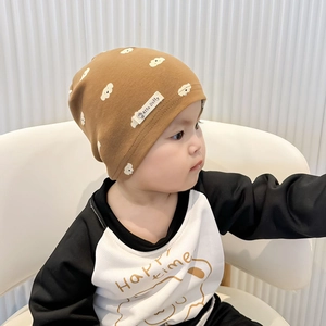 Close-up of a brown knit baby beanie with cloud prints and a Happy Time printed shirt