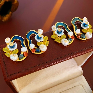 Detailed close-up of vintage flower earrings with pearls and blue enamel on brown leather