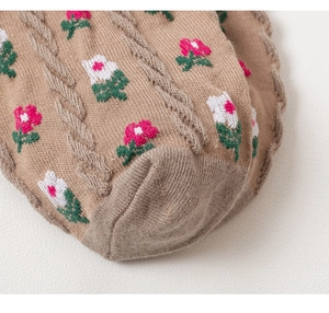 Detailed close-up of floral embroidery and cable knit texture on beige crew socks