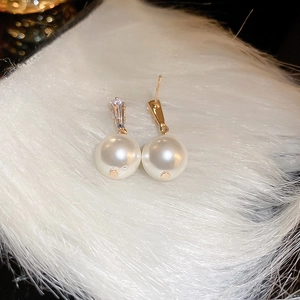 Detailed close-up of small pearl earrings with diamond accents on a soft texture