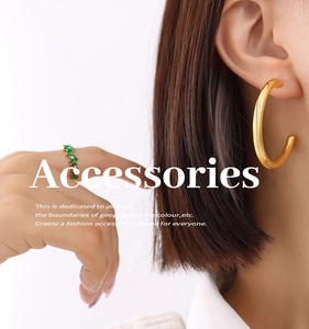 Close-up of golden hollow C-shaped hoop earrings and green gemstone ring on a model