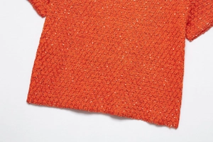 Dettaglio del top in maglia arancione con paillettes dorate e trama del tessuto fitta