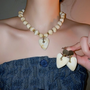 Close-up of cream acrylic heart pendant necklace and matching earrings on a female model