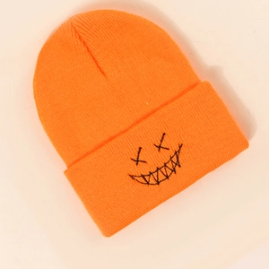 Detail shot of bright orange knit beanie featuring black embroidered funny face expression
