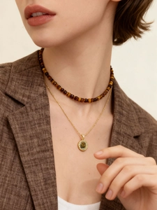 Detail view of gold-plated tiger eye beaded necklace with pendant layered on a model