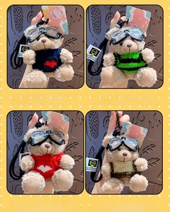 Detail of four teddy bear plush keychains wearing goggles and various knit sweaters