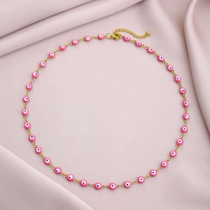 Detail of gold evil eye necklace with pink beads on a soft silk background