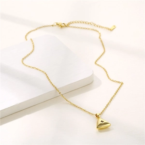 Gold stainless steel triangle necklace with a central zircon stone on white marble