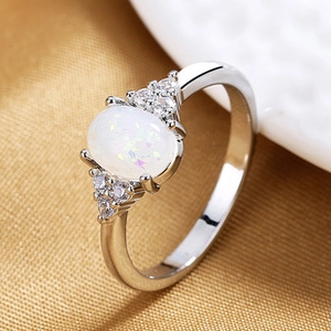 Detailed macro view of an oval white opal ring with small side zircons on a gold fabric