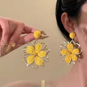 Vue détaillée de boucles d'oreilles fleurs tressées jaunes avec bords dorés