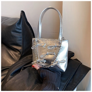 Detail of silver handbag featuring decorative bows and a delicate pearl chain strap