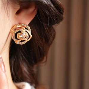 Detailed view of a gold hollow rose earring with sparkling crystals on a model's ear