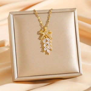 Elegant gold bow necklace with leaf-shaped zircon pendant displayed on champagne silk fabric