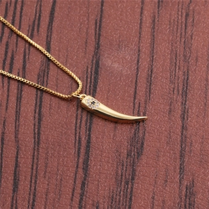 Golden horn pendant necklace featuring evil eye detail on textured brown backdrop